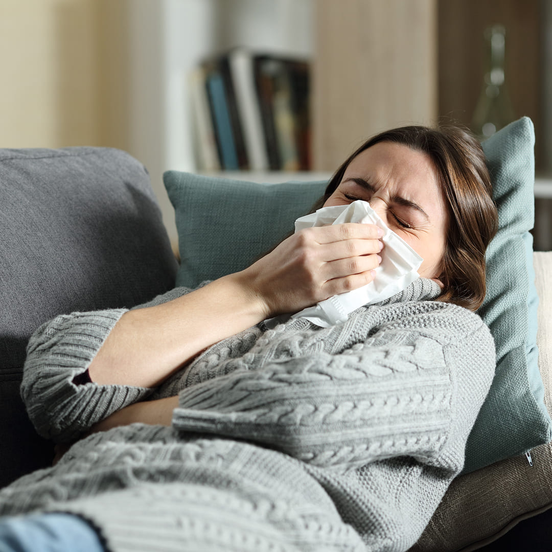 Donna sul divano che starnutisce con un fazzoletto &mdash; sintomi da Virus Respiratorio Sinciziale, infezione delle vie respiratorie negli adulti